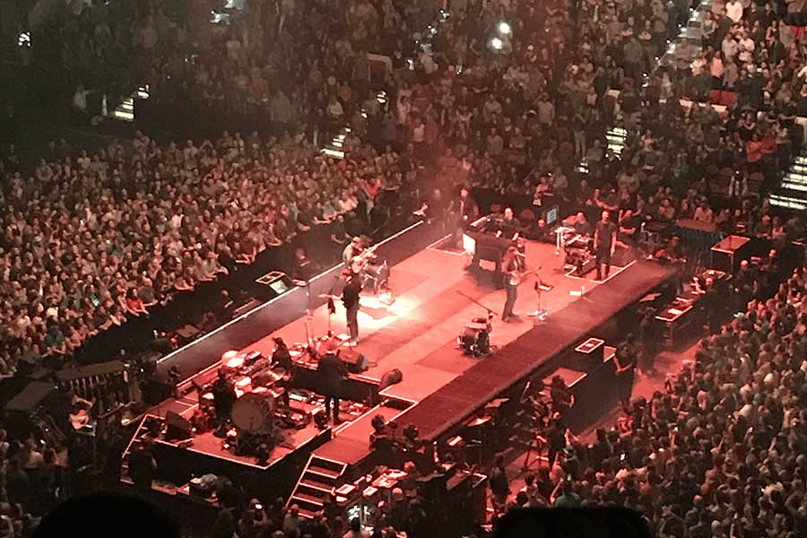 Photo of Coliseum venue filled with an audience listening to music. Musicians on the stage.