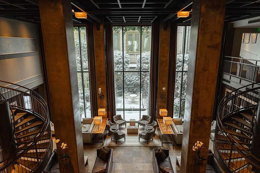 Proximity Hotel Social Lobby | Photos by Griffin Hart Davis Photography The Proximity Hotel lobby as seen from the first floor features two spiral staircases, 22 foot tall windows, and gathering spaces for friends and family.